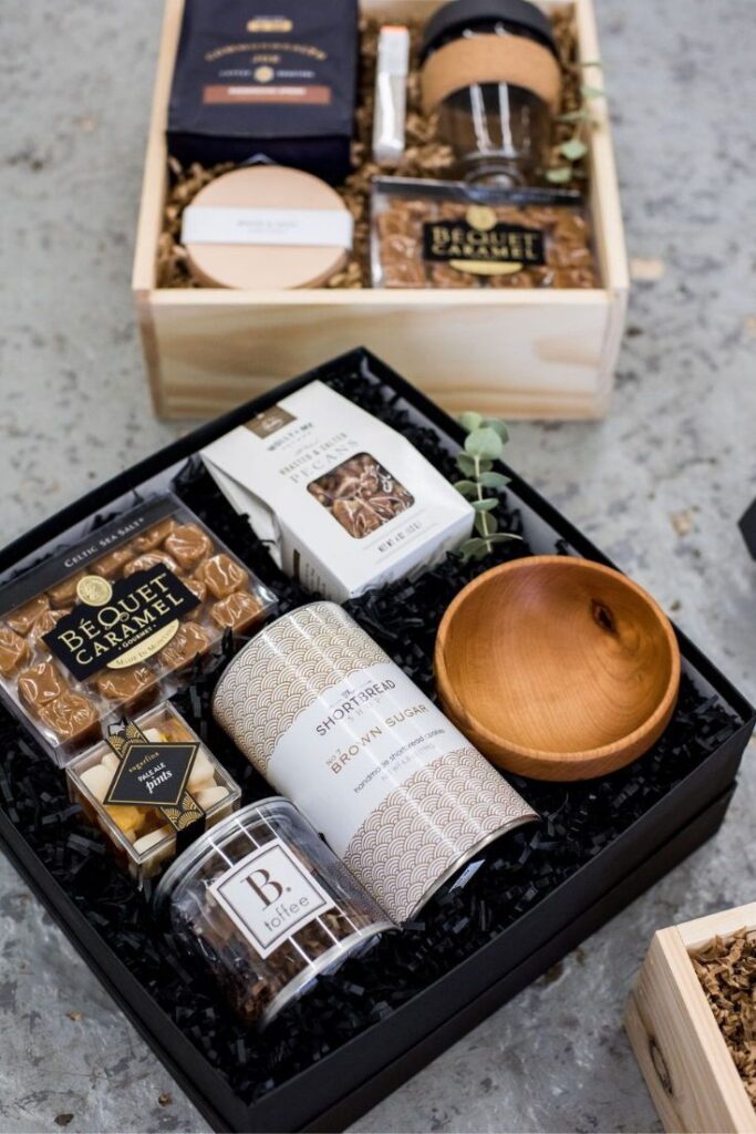 Gift boxes with gourmet treats, including caramel, shortbread, toffee, and a wooden bowl, arranged elegantly.