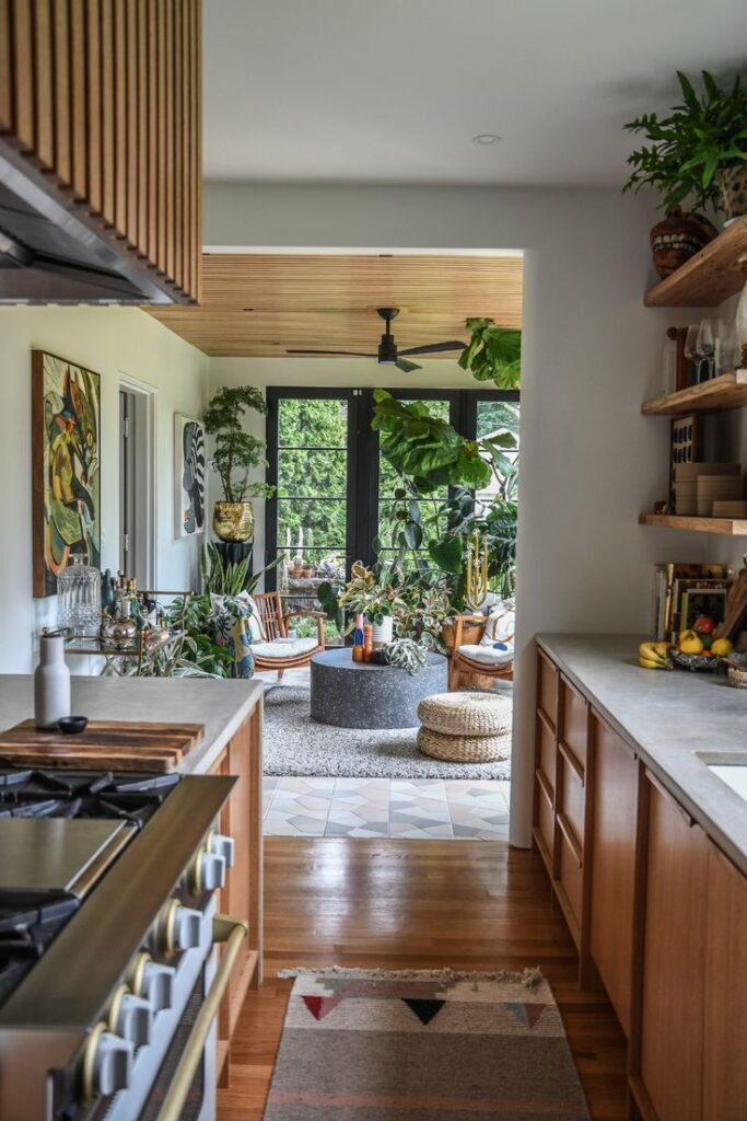 053a43c5bcc1247eafe6191ea8ca75b1 Modern open-plan kitchen leading to a cozy sunroom filled with houseplants and stylish decor. | Sky Rye Design Modern open-plan kitchen leading to a cozy sunroom filled with houseplants and stylish decor.