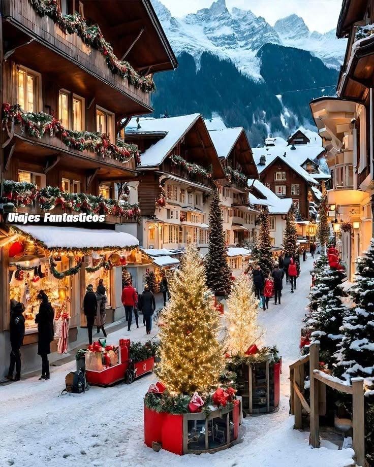 0798ae14-df73-4ee7-9517-243371f09c75 Snowy alpine village decorated for Christmas with festive lights, people strolling, and mountains in the background. | Sky Rye Design Snowy alpine village decorated for Christmas with festive lights, people strolling, and mountains in the background.