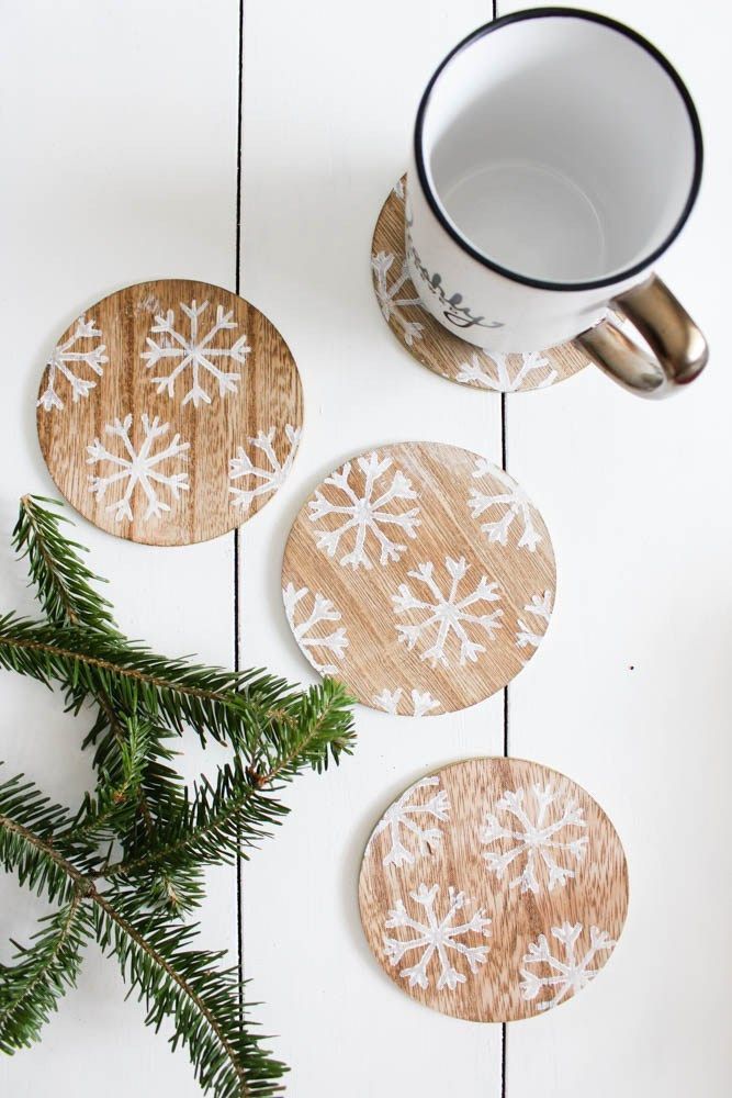 0995e6e7-1c56-4df7-a6e5-2f1c2b8f8f02 Rustic wooden coasters with snowflake designs next to a mug and pine branch on a white tabletop. | Sky Rye Design Rustic wooden coasters with snowflake designs next to a mug and pine branch on a white tabletop.