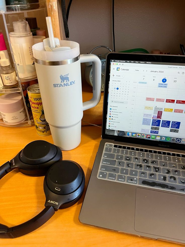 0bb6ba0aaccb2fe0c8e8153fe0296583 Laptop with calendar, Stanley tumbler, and Sony headphones on a wooden desk. | Sky Rye Design Laptop with calendar, Stanley tumbler, and Sony headphones on a wooden desk.