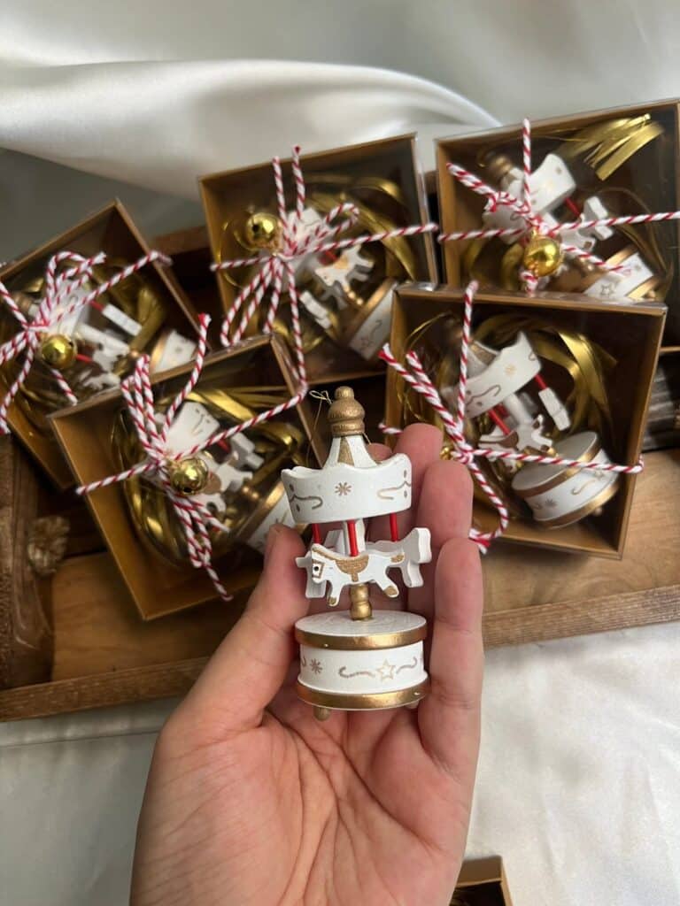 Hand holding a miniature carousel ornament with packaged decorations in background.