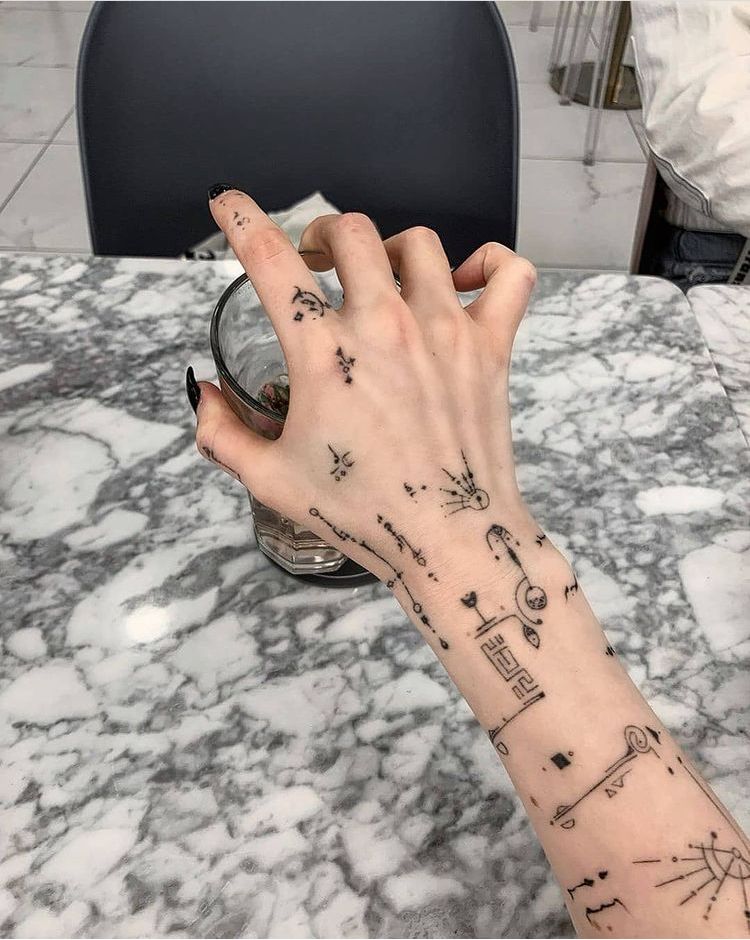 Hand with geometric tattoos holding a glass on a marble table.