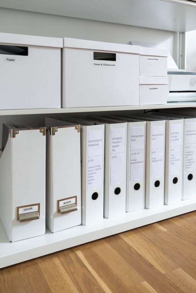 Organized white office binders and storage boxes on shelves for efficient document management.