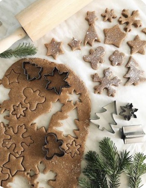 Gingerbread dough with holiday cookie cutters and pine branches on a marble surface, ready for baking festive treats.