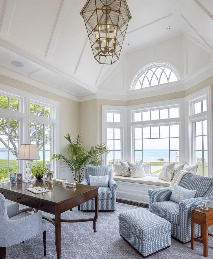 Bright coastal living room with armchairs, a wooden desk, large windows, and ocean view, highlighting serene elegance.