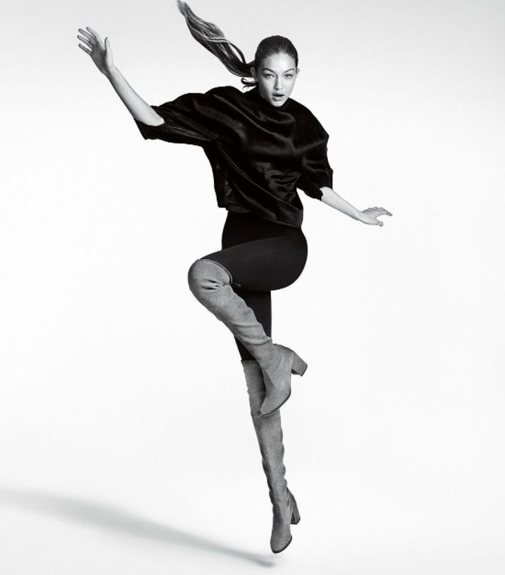 Fashion model in dynamic pose, wearing black sweater and thigh-high boots, against a white background.