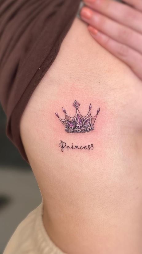 _ 1 Crown and Princess tattoo on a person's side, with purple and gem details, close-up view. | Sky Rye Design Crown and Princess tattoo on a person's side, with purple and gem details, close-up view.