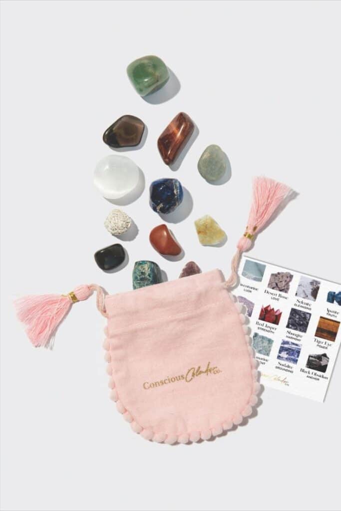 Assorted healing crystals with a pink pouch and identification card, includes amethyst, quartz, and jasper stones.