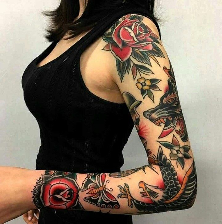 Colorful sleeve tattoo featuring roses, a wolf, and a butterfly on a woman's arm in a black tank top.