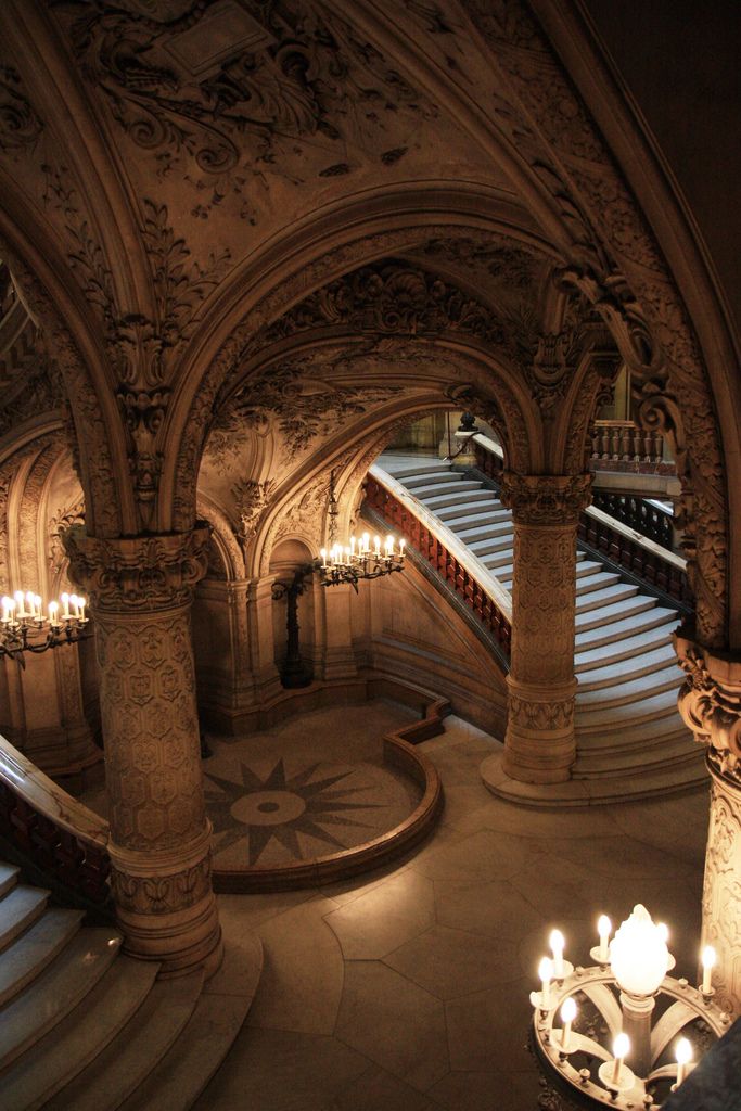 Ornate grand staircase with intricately carved arches and elegant chandeliers in a historic building.