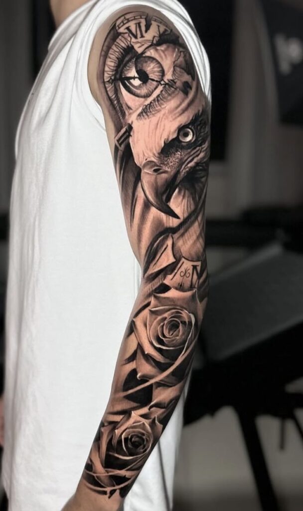 Detailed sleeve tattoo with a clock, eye, raven, and roses on a person's arm in a white shirt.