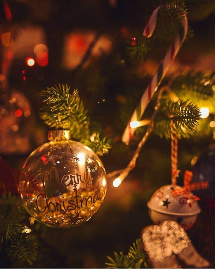 Christmas tree with a Merry Christmas ornament, candy cane, and twinkling lights creating a warm festive glow.