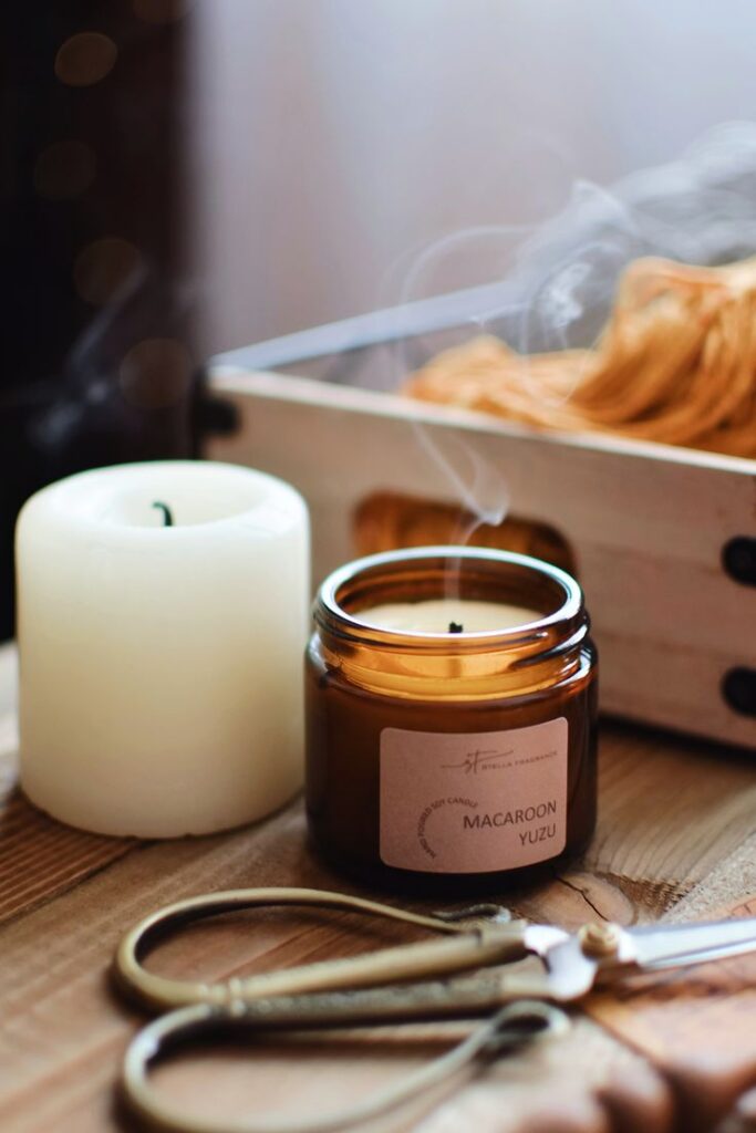 _ 10 Cozy scene with lit Macaroon Yuzu candle, scissors, and wooden box on table, creating a warm ambiance. | Sky Rye Design Cozy scene with lit Macaroon Yuzu candle, scissors, and wooden box on table, creating a warm ambiance.