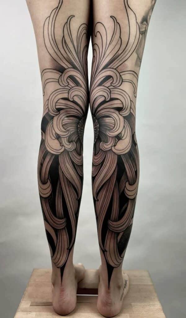 _ 10 Intricate black and beige floral leg tattoo with flowing patterns on both calves. | Sky Rye Design Intricate black and beige floral leg tattoo with flowing patterns on both calves.