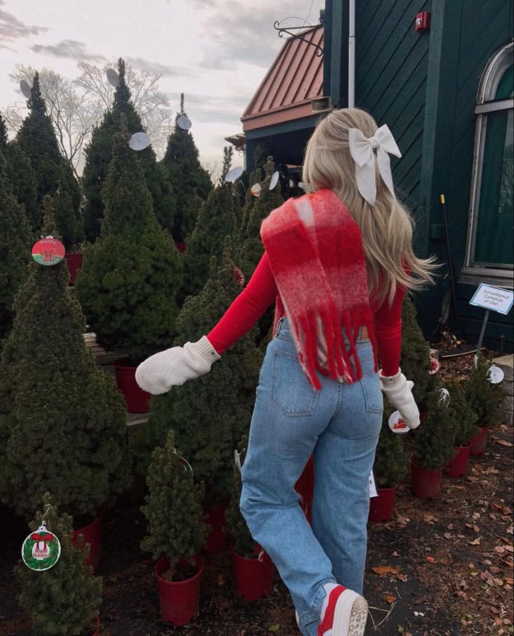 10c70fac-aebb-4588-92eb-4d9458aa6223 Woman in festive outfit exploring Christmas tree farm, wearing a red sweater, scarf, jeans, and white bow. | Sky Rye Design Woman in festive outfit exploring Christmas tree farm, wearing a red sweater, scarf, jeans, and white bow.