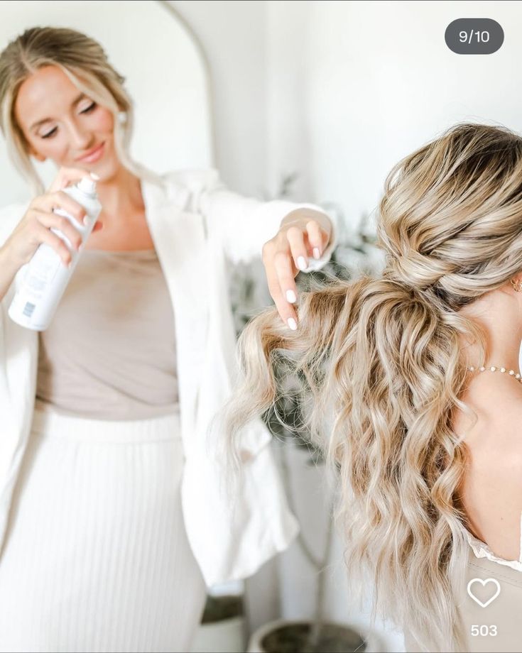 Hairstylist applying hairspray to long, wavy blonde hair in a light, modern salon setting.