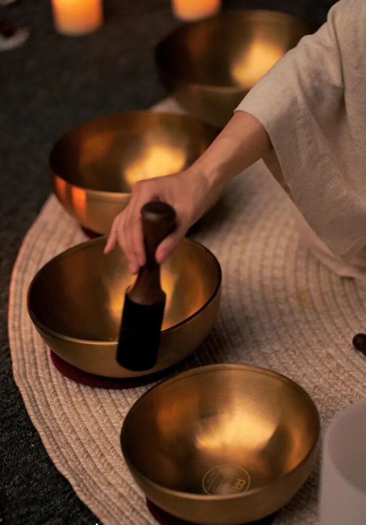 Hand playing Tibetan singing bowl for meditation amid candlelit ambiance.