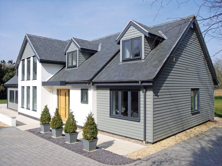 Modern two-story house with gray cladding, large windows, and potted plants lining the entrance path.