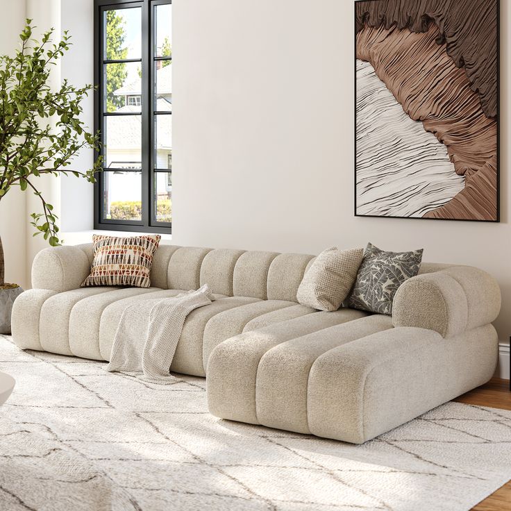 Modern beige sectional sofa in bright living room, with abstract wall art and large window view.