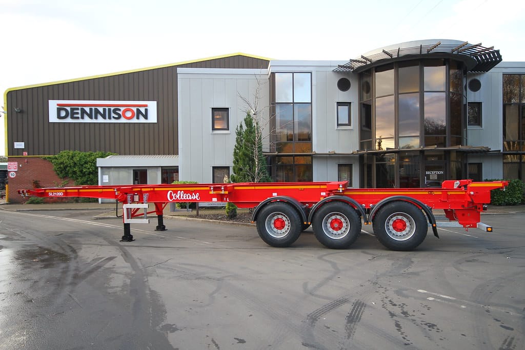 Red trailer parked in front of modern industrial building with large glass windows and signage.