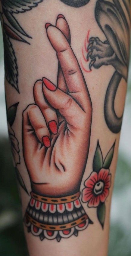 Tattoo of a hand with red nails crossed fingers, surrounded by floral and abstract designs.