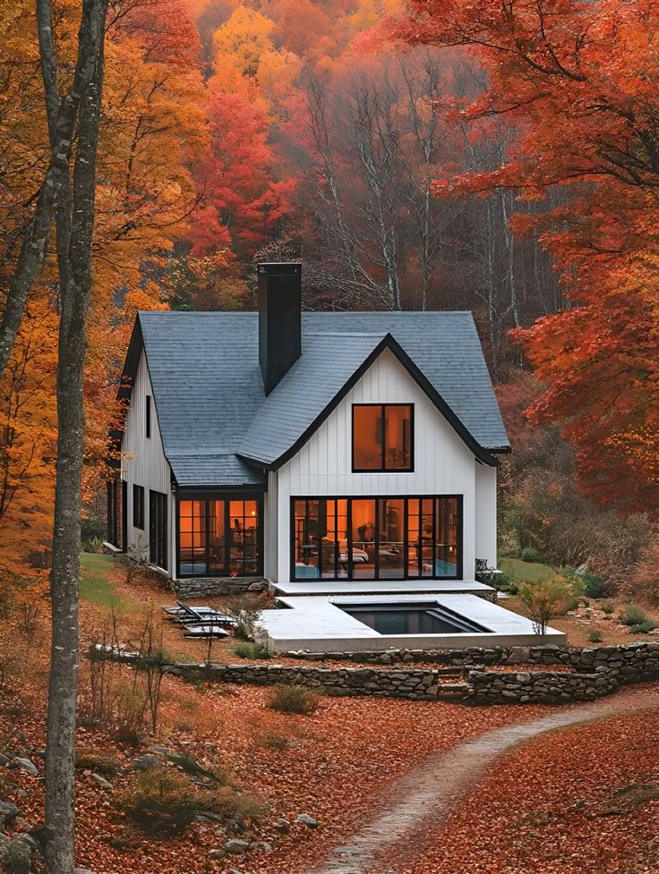 Modern house in vibrant autumn forest, with large windows and a pool, surrounded by colorful fall foliage.