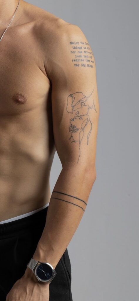 Arm tattoos with minimalist line art and script, alongside a minimalist watch on a muscular male arm.