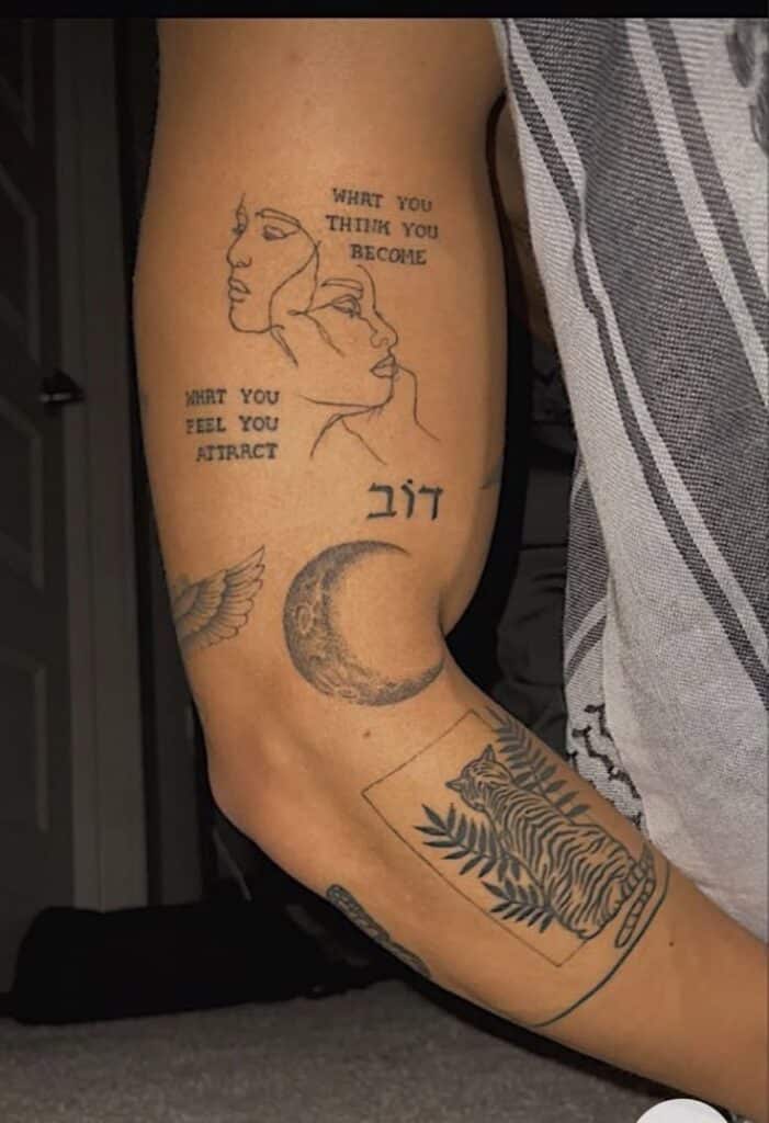 Arm tattoos featuring quotes, faces, crescent moon, tiger, leaf, and symbols expressing creativity and inspiration.
