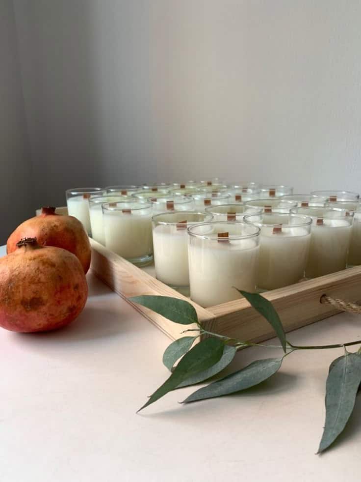 _ 14 Wooden tray with candles, two pomegranates, and green leaves on a white surface. Cozy home decor setting. | Sky Rye Design Wooden tray with candles, two pomegranates, and green leaves on a white surface. Cozy home decor setting.