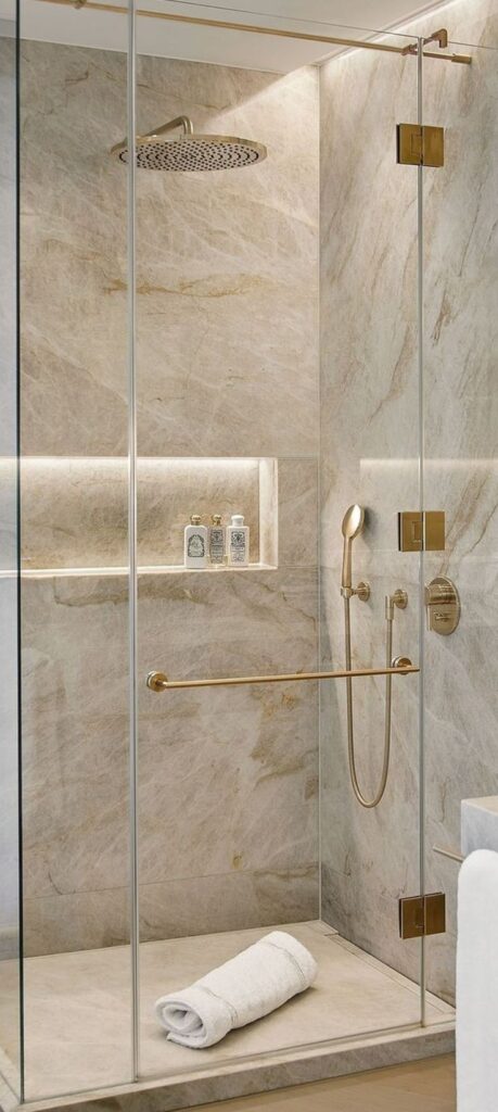 _ 14 Luxurious marble shower with gold fixtures, rain showerhead, and glass doors, accented with a rolled white towel. | Sky Rye Design Luxurious marble shower with gold fixtures, rain showerhead, and glass doors, accented with a rolled white towel.