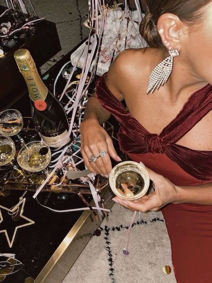 Woman in red dress at a festive party, holding a champagne glass with decorations and a champagne bottle on the table.