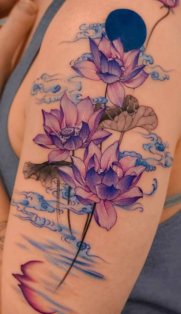 _ 14 Vibrant purple lotus flower tattoo with blue accents on arm, featuring clouds and water reflections. | Sky Rye Design Vibrant purple lotus flower tattoo with blue accents on arm, featuring clouds and water reflections.