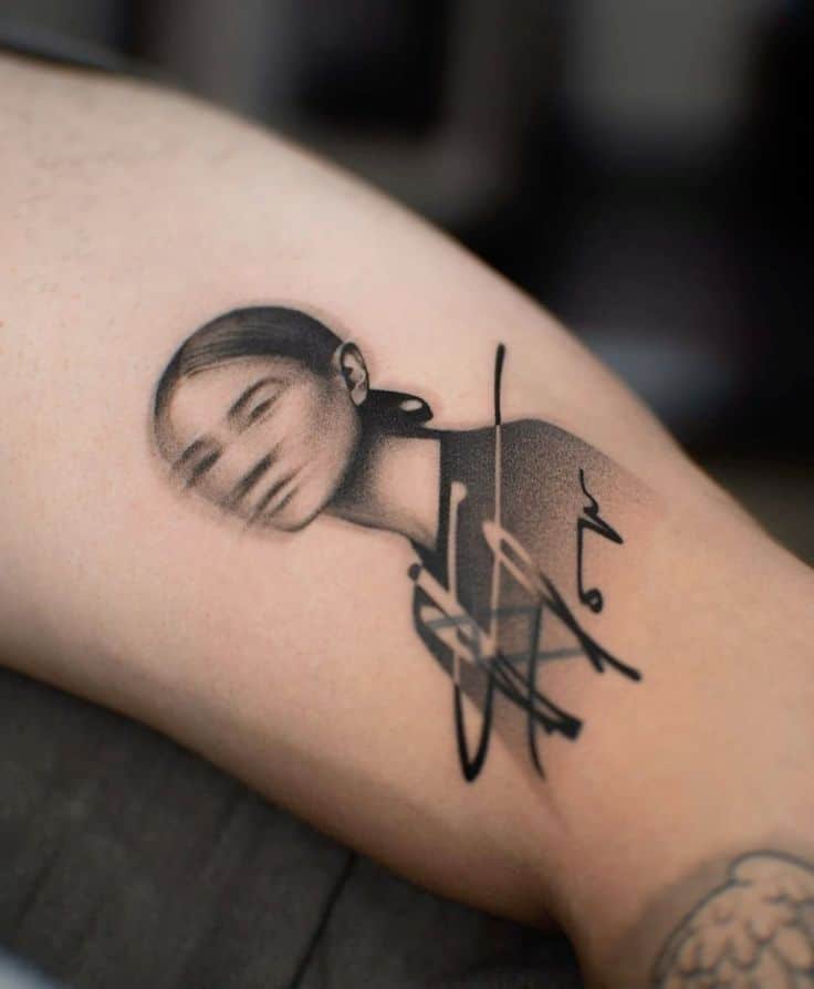 Blurred portrait tattoo with abstract elements in black ink on the upper arm.
