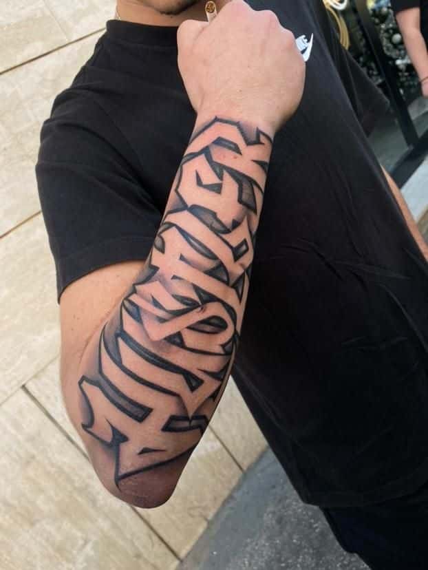 Forearm tattoo with bold, black geometric design on a person wearing a dark t-shirt.