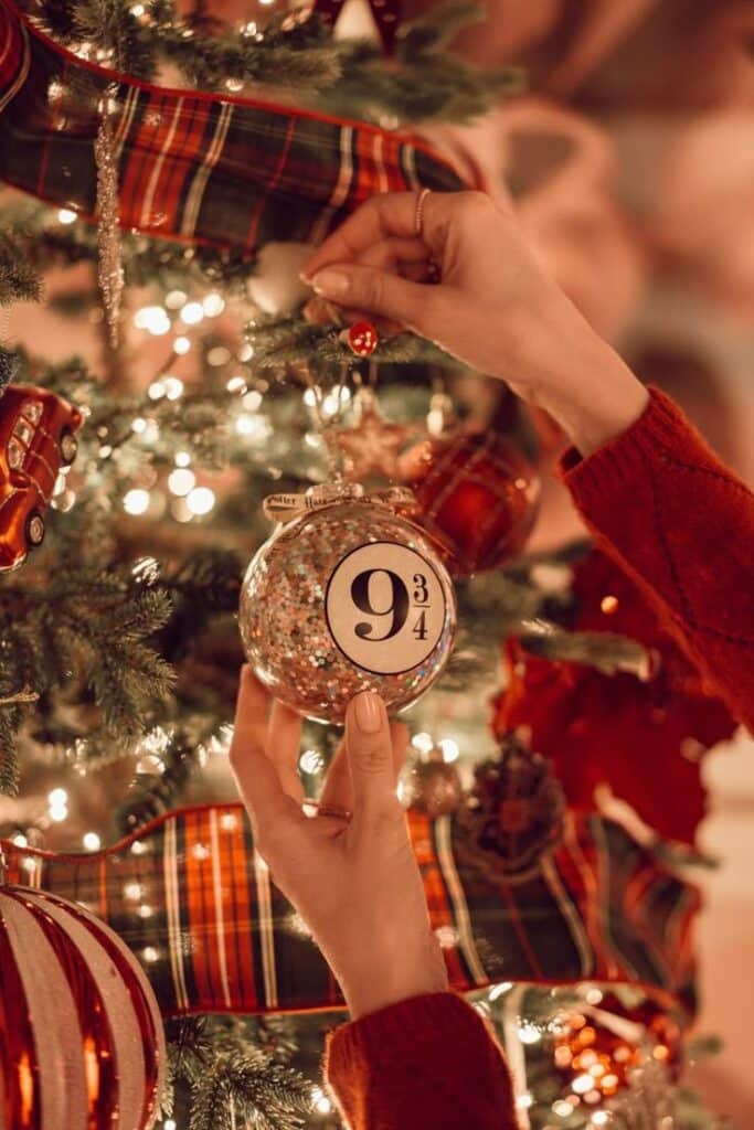 _ 15 Hands decorating a Christmas tree with a magical theme ornament, adding festive charm and warm lights. | Sky Rye Design Hands decorating a Christmas tree with a magical theme ornament, adding festive charm and warm lights.
