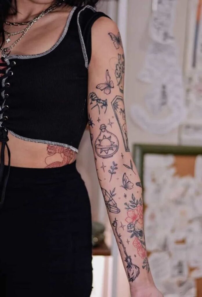 Tattooed arm with floral and butterfly designs, woman in black top, standing indoors.