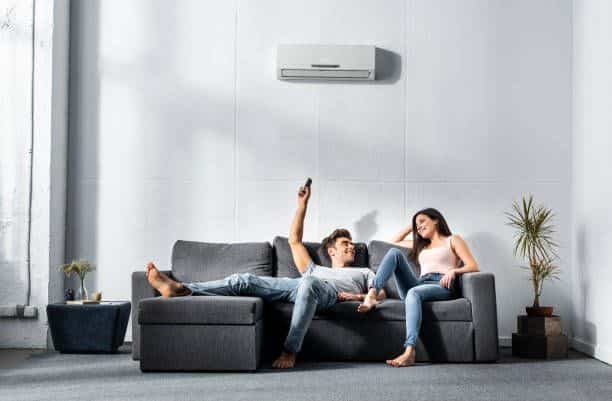 Couple relaxing on a sofa under an air conditioner, enjoying a cozy time indoors.