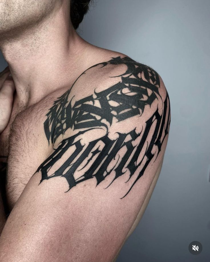 Intricate black tribal script tattoo on a person's shoulder, bold design, detailed lines, artistic expression.