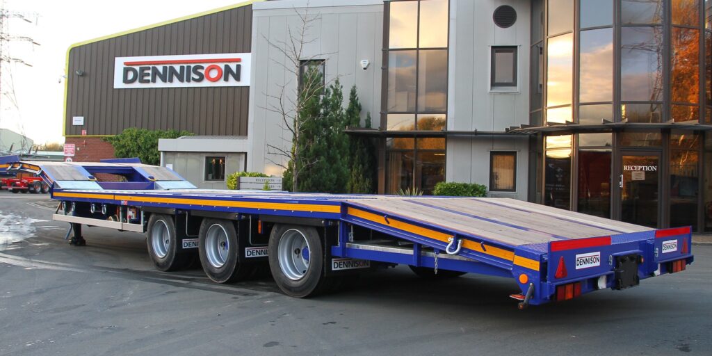 Flatbed trailer in front of the Dennison factory, showcasing industrial design and heavy-duty capacity.