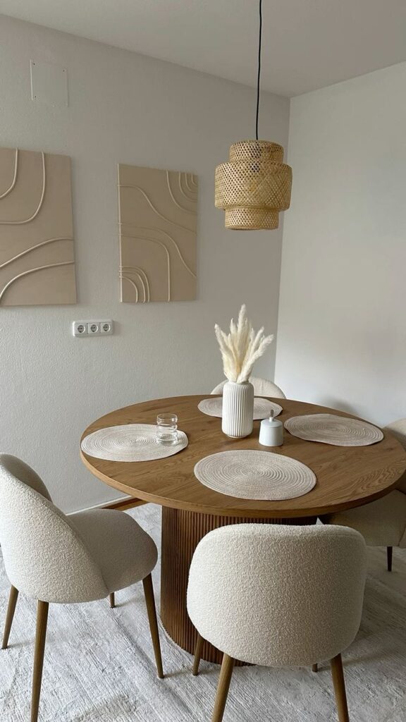 15fd9dda18fb76c933f932a98f65c233 Modern dining room with round wooden table, beige chairs, pampas grass vase, and textured wall art. | Sky Rye Design Modern dining room with round wooden table, beige chairs, pampas grass vase, and textured wall art.