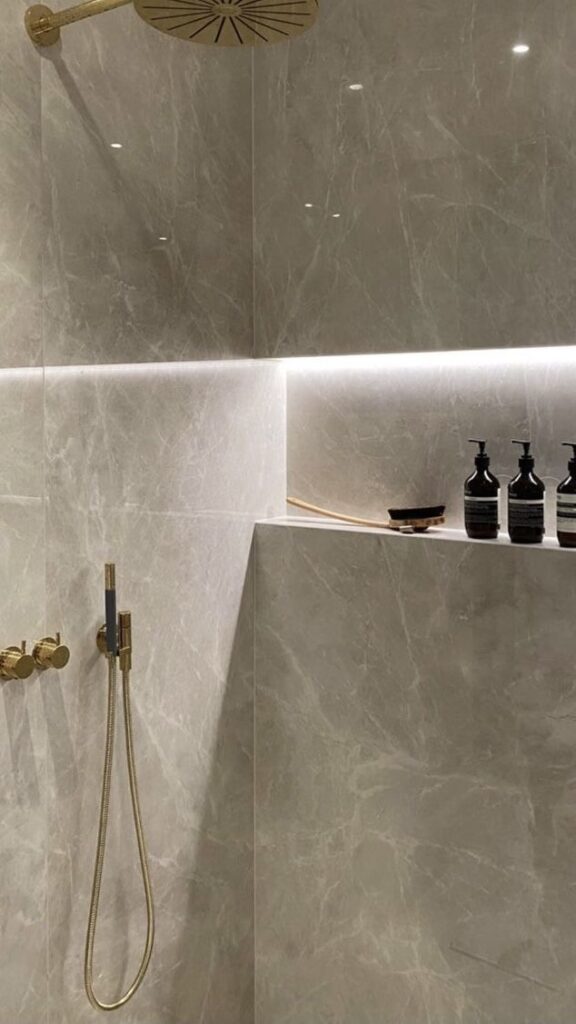 _ 16 Luxurious marble shower with gold fixtures, LED lighting, and dark shampoo bottles on a shelf for an elegant bathroom design. | Sky Rye Design Luxurious marble shower with gold fixtures, LED lighting, and dark shampoo bottles on a shelf for an elegant bathroom design.