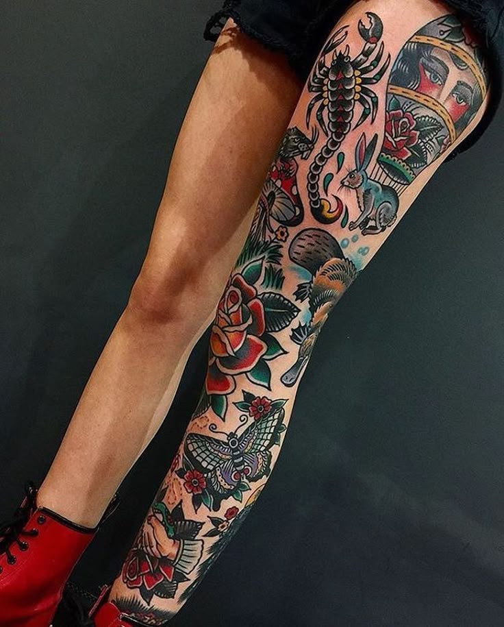 Colorful full-leg tattoo featuring scorpion, flowers, and animals on person with red boots sitting against a dark background.