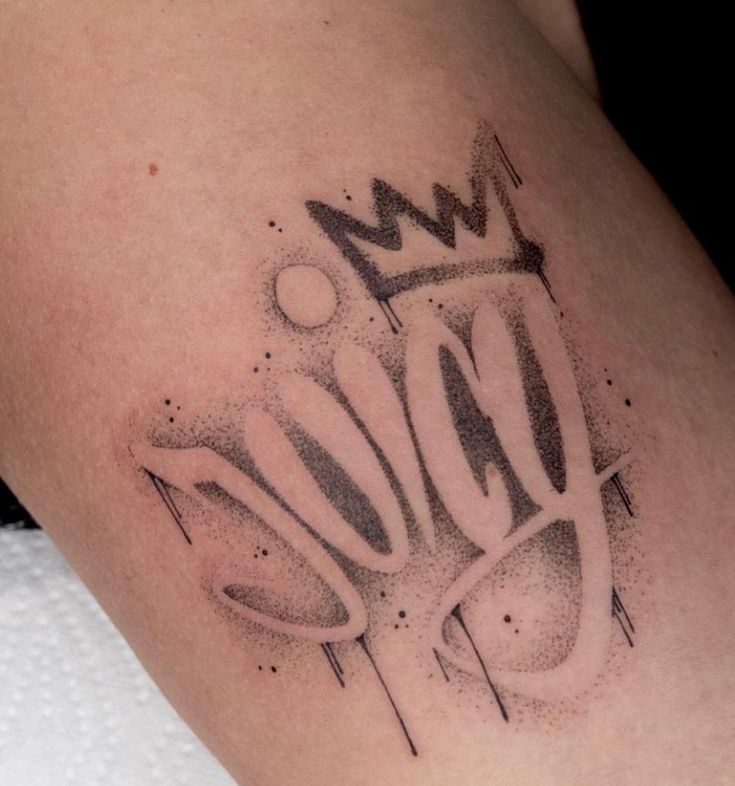 Tattoo of the word juicy with a crown design, featuring a bold graffiti-style on skin.