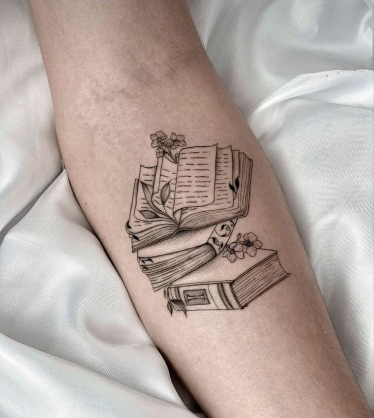 _ 16 Tattoo of stacked books with flowers on forearm, showcasing a love for literature and art. | Sky Rye Design Tattoo of stacked books with flowers on forearm, showcasing a love for literature and art. Book Tattoo