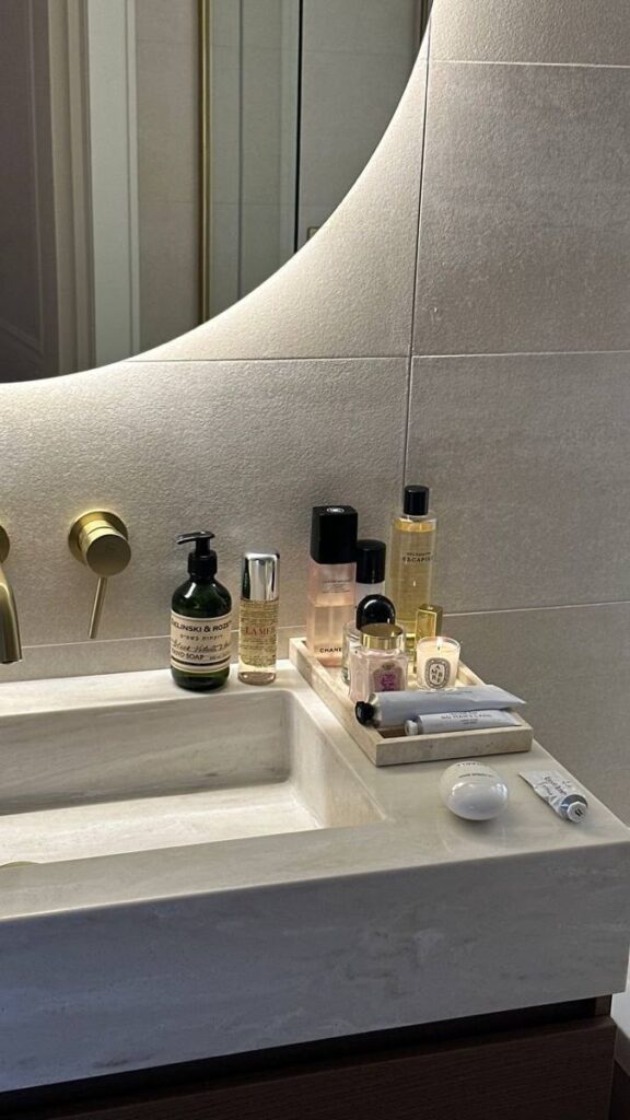 _ 17 Luxurious bathroom vanity with skincare products and modern gold faucet on a sleek marble countertop. | Sky Rye Design Luxurious bathroom vanity with skincare products and modern gold faucet on a sleek marble countertop.