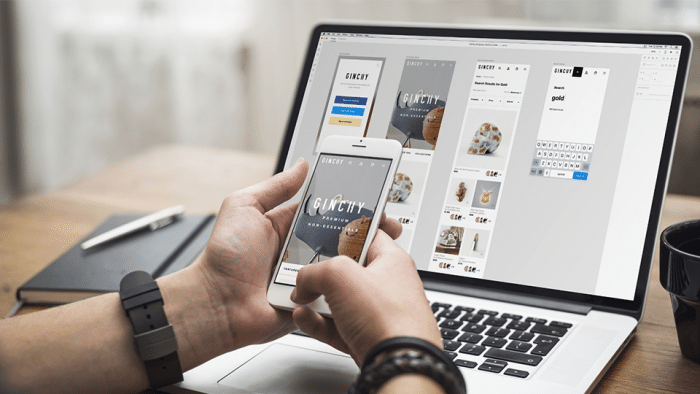 1_62ZZ3SF414j6aSMzjqEldQ Person using phone and laptop for mobile web design, showcasing a responsive layout. | Sky Rye Design Person using phone and laptop for mobile web design, showcasing a responsive layout.