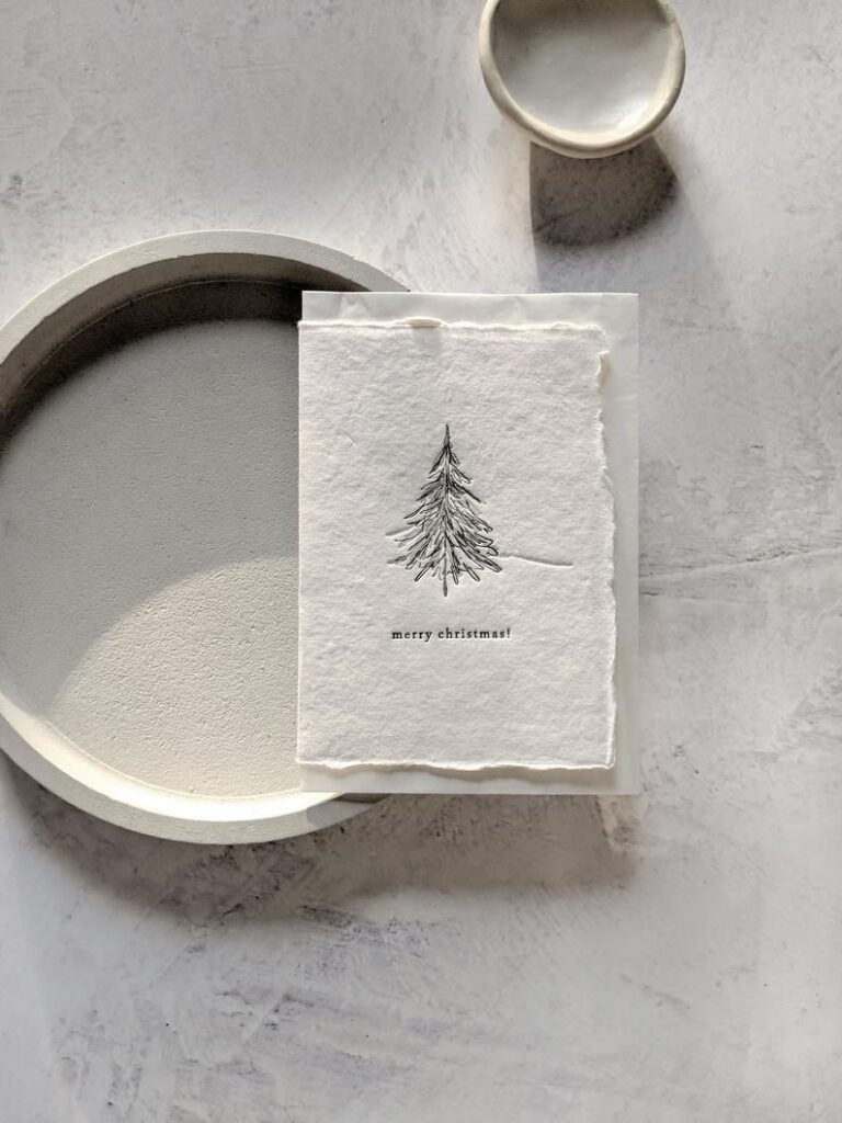1a2d0a9a09bf789bba30b063e5f307fc Minimalist Christmas card with tree sketch on textured paper, placed on round plates on a marble surface. | Sky Rye Design Minimalist Christmas card with tree sketch on textured paper, placed on round plates on a marble surface.