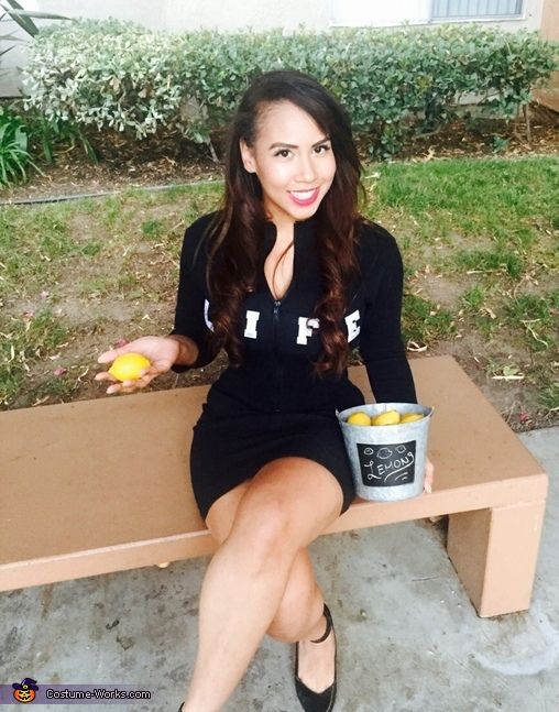 Woman dressed as Life holding lemons while sitting on a bench, depicting When life gives you lemons metaphor.