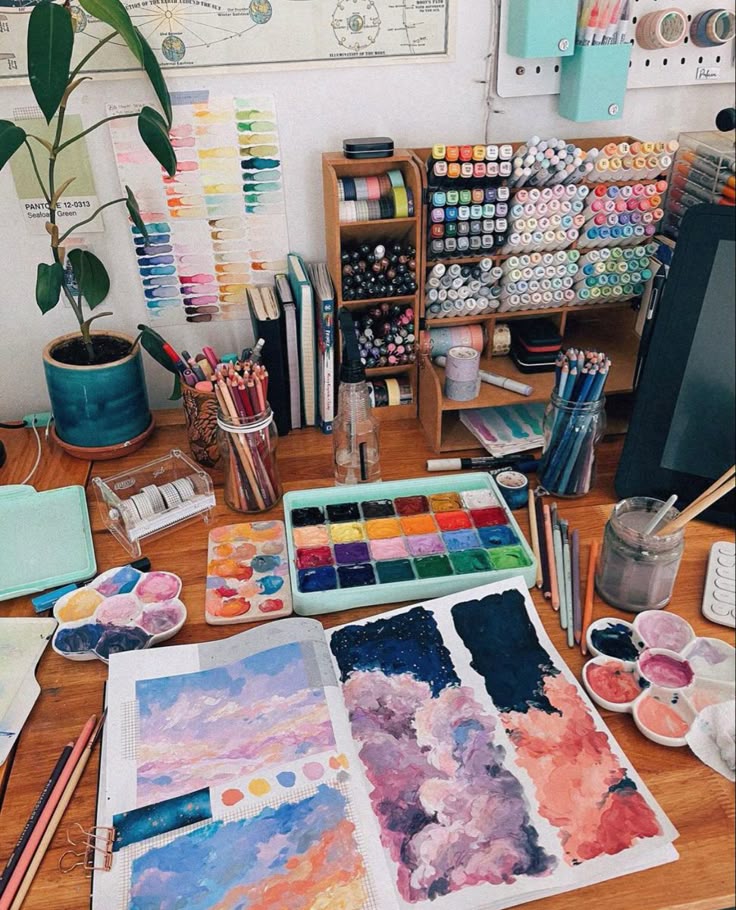 Creative art desk with paints, markers, pencils, and a sketchbook featuring colorful cloud paintings. Perfect artistic workspace.